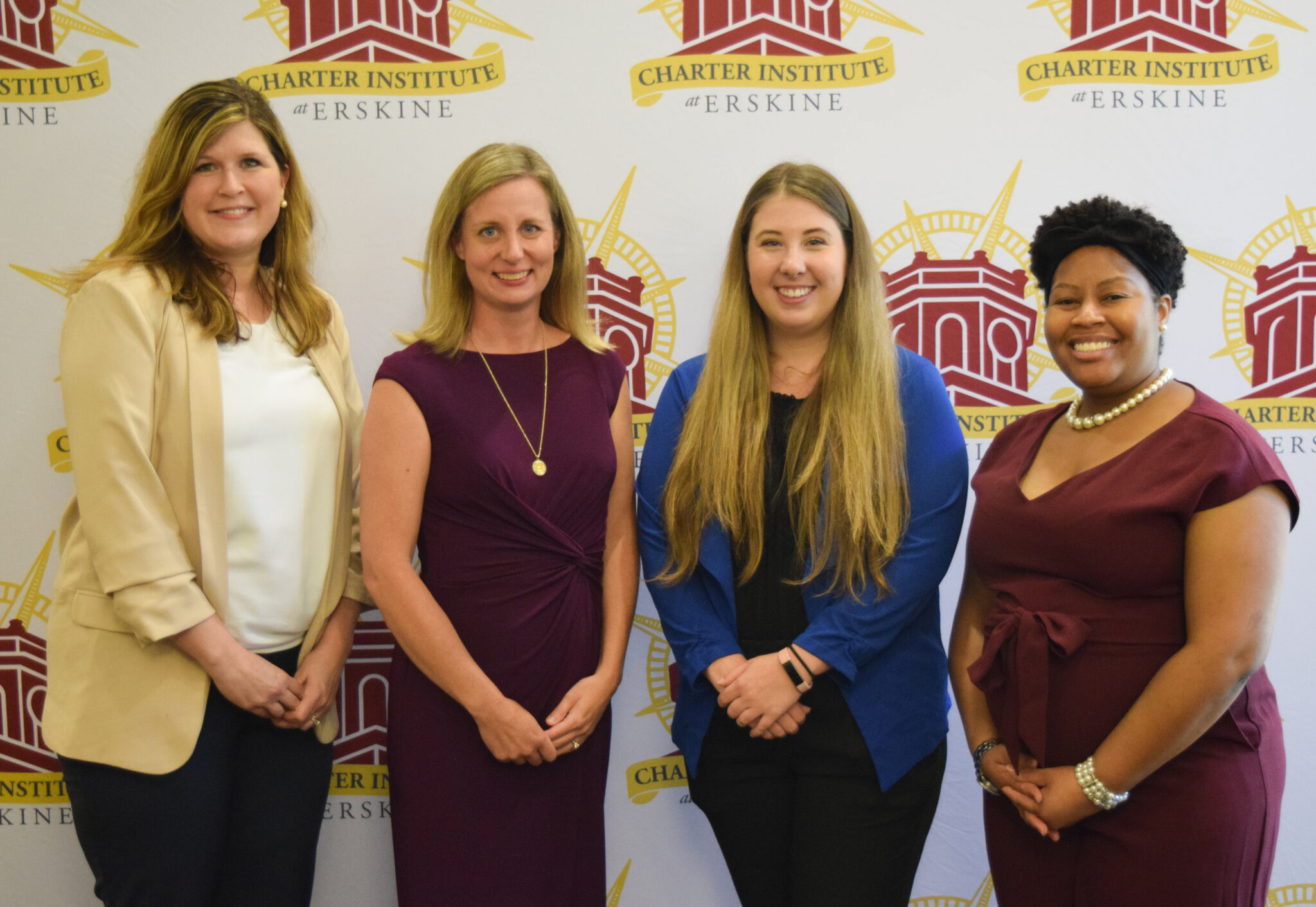 Four women in business attire in front of the Erskine Charter backdrop.