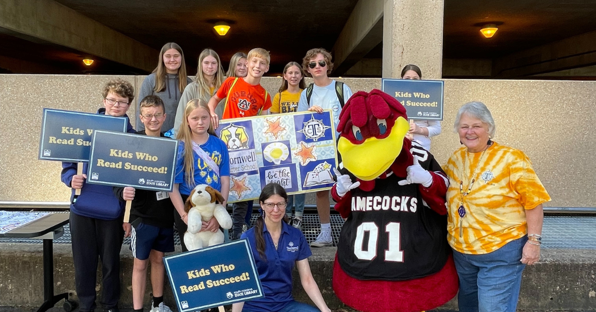 a group of people and mascot holding signs including one that says kids who read succeed